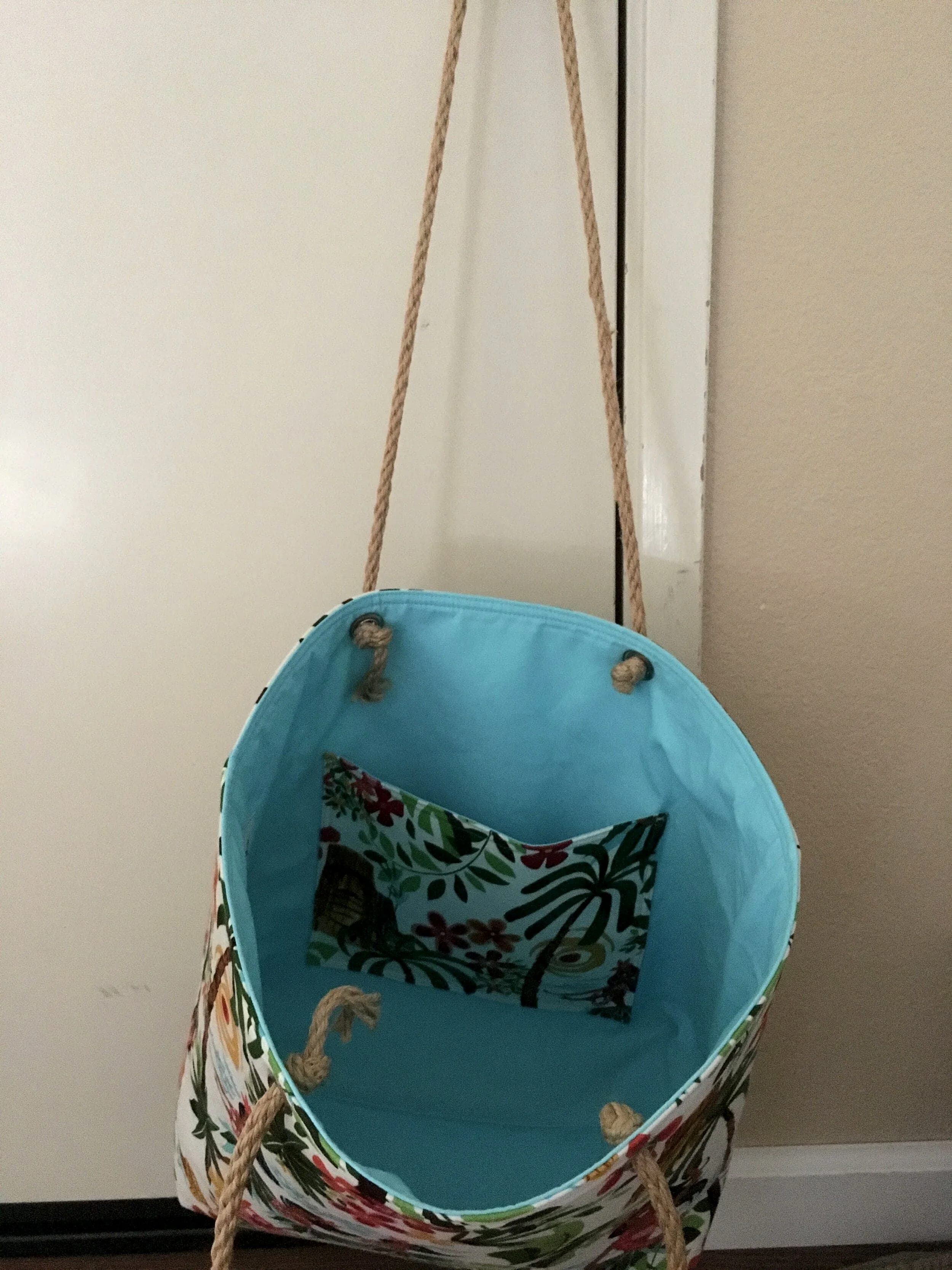 Hula-print tote hanging open from its rope handles, turquoise lining and interior patch pocket visible