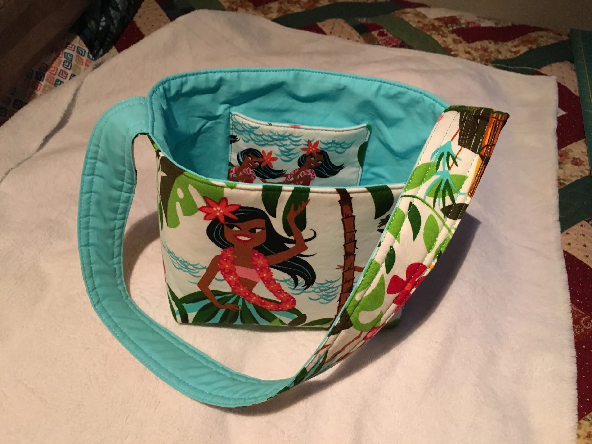Hula-print tote with quilted turquoise handles and lining, lying on a pale quilt