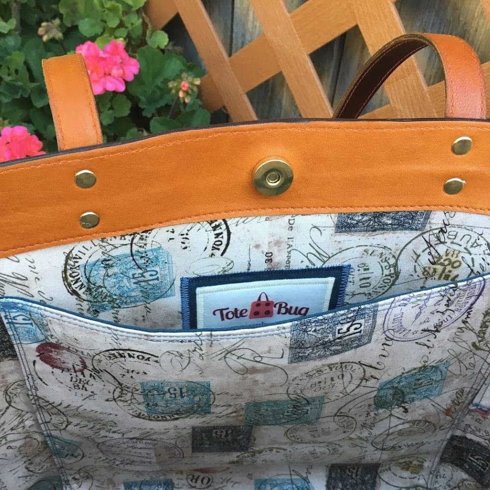 Interior of a leather tote showing the map-print lining, brass snap closure and Totebug label