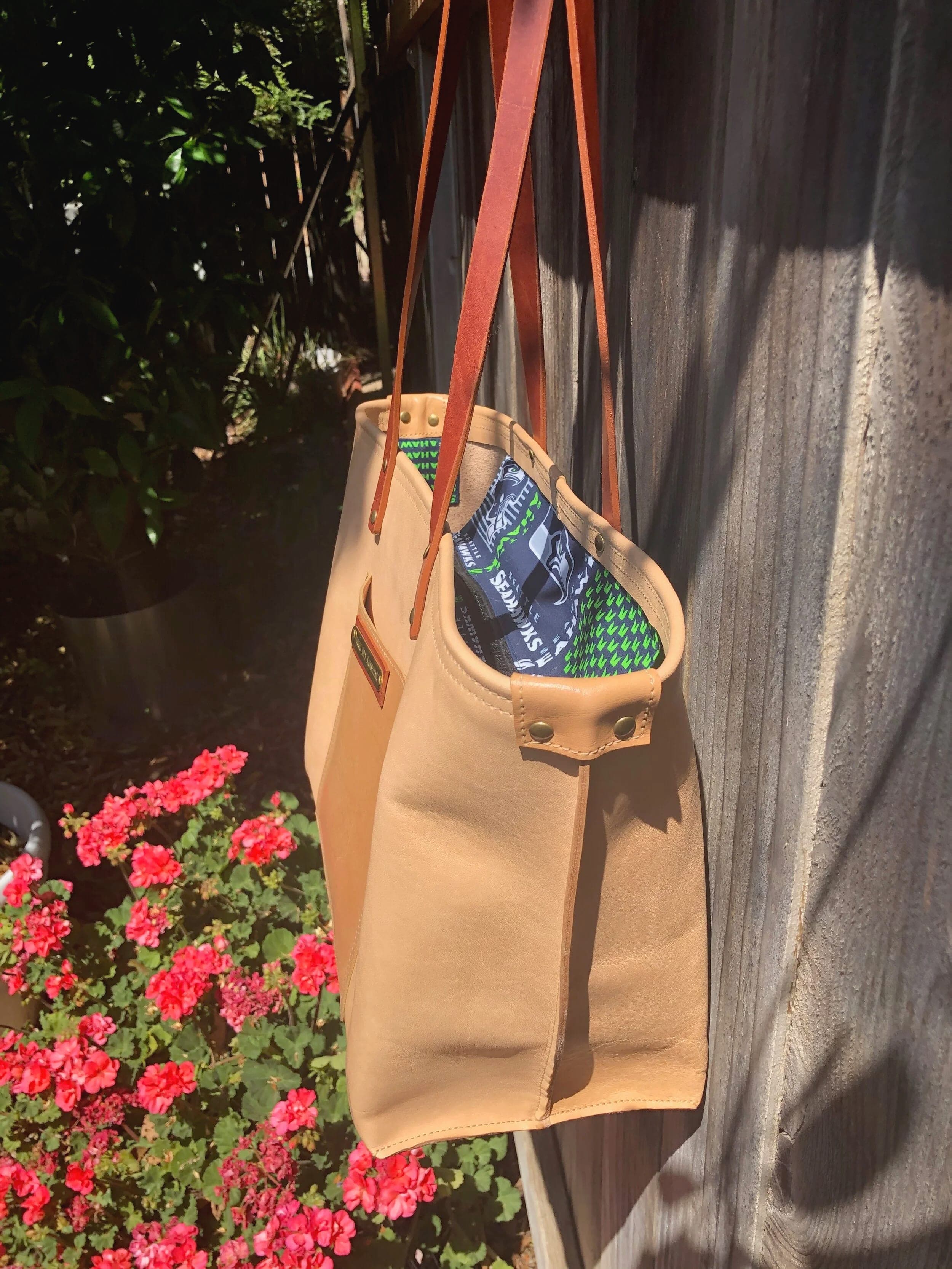 Natural tan leather tote hanging on a fence, its patterned interior lining showing