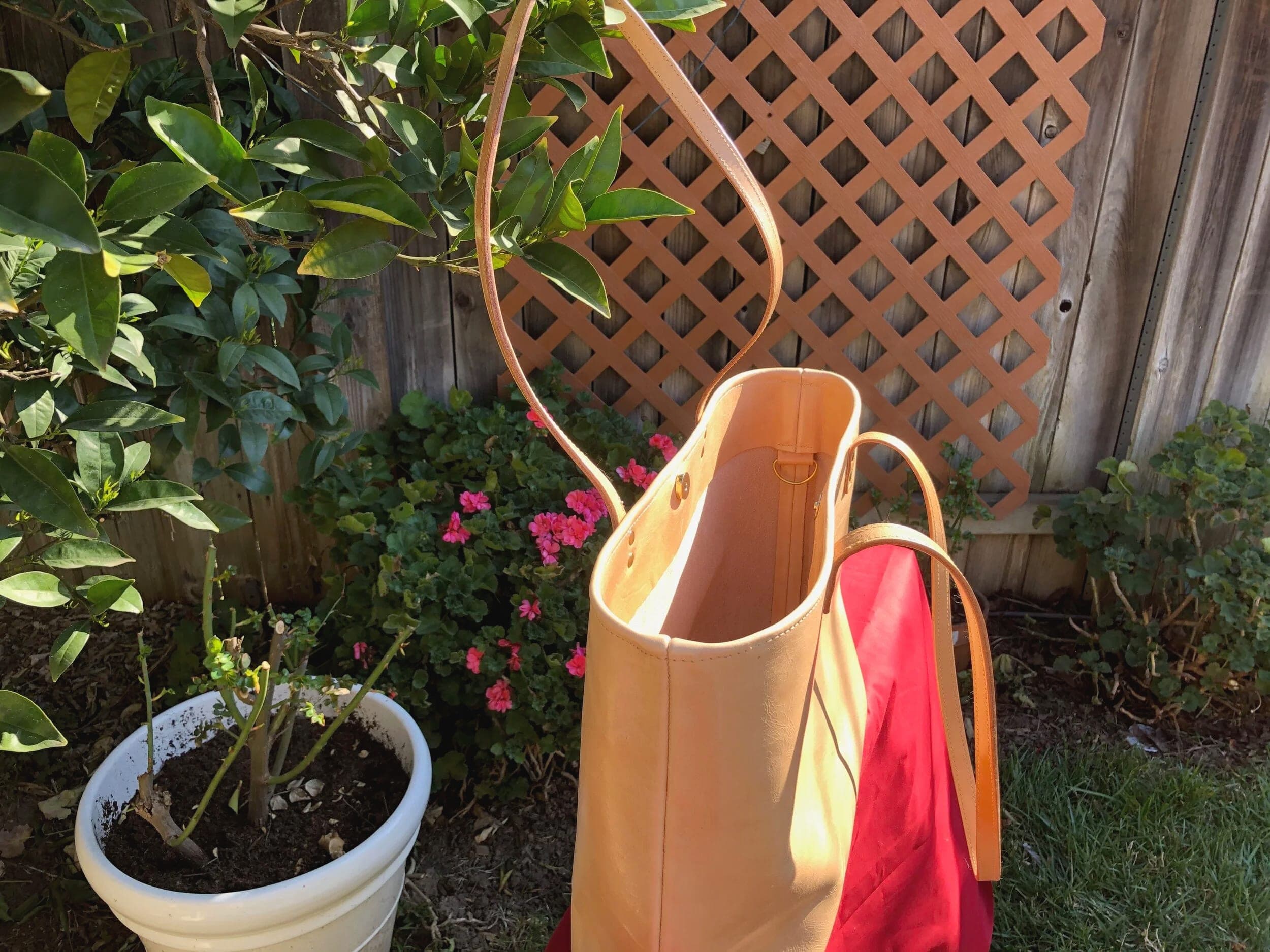 Two natural tan leather totes on a lattice fence beside a potted plant