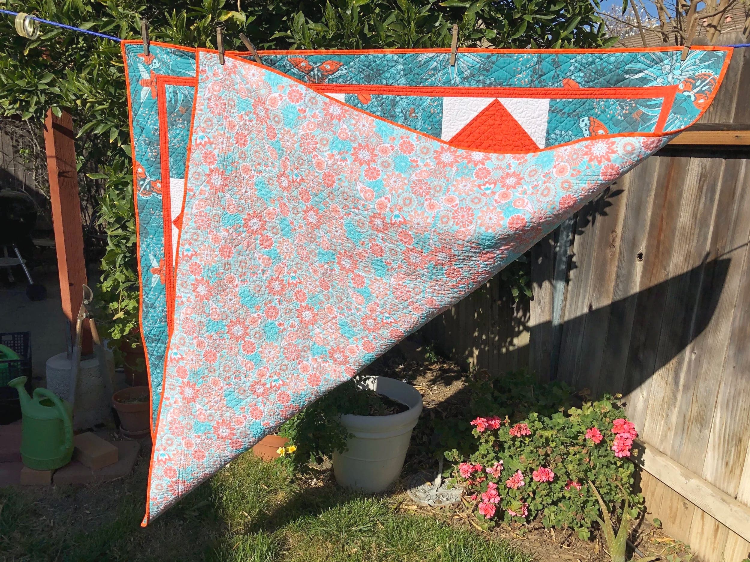 Quilt folded back to show its pale pink and teal floral reverse, hanging outdoors