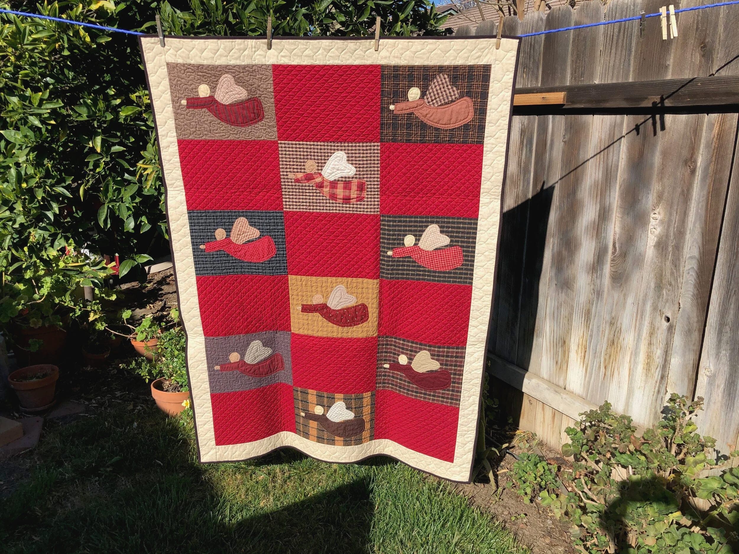 Red and cream quilt appliquéd with birds, hanging against a wooden fence