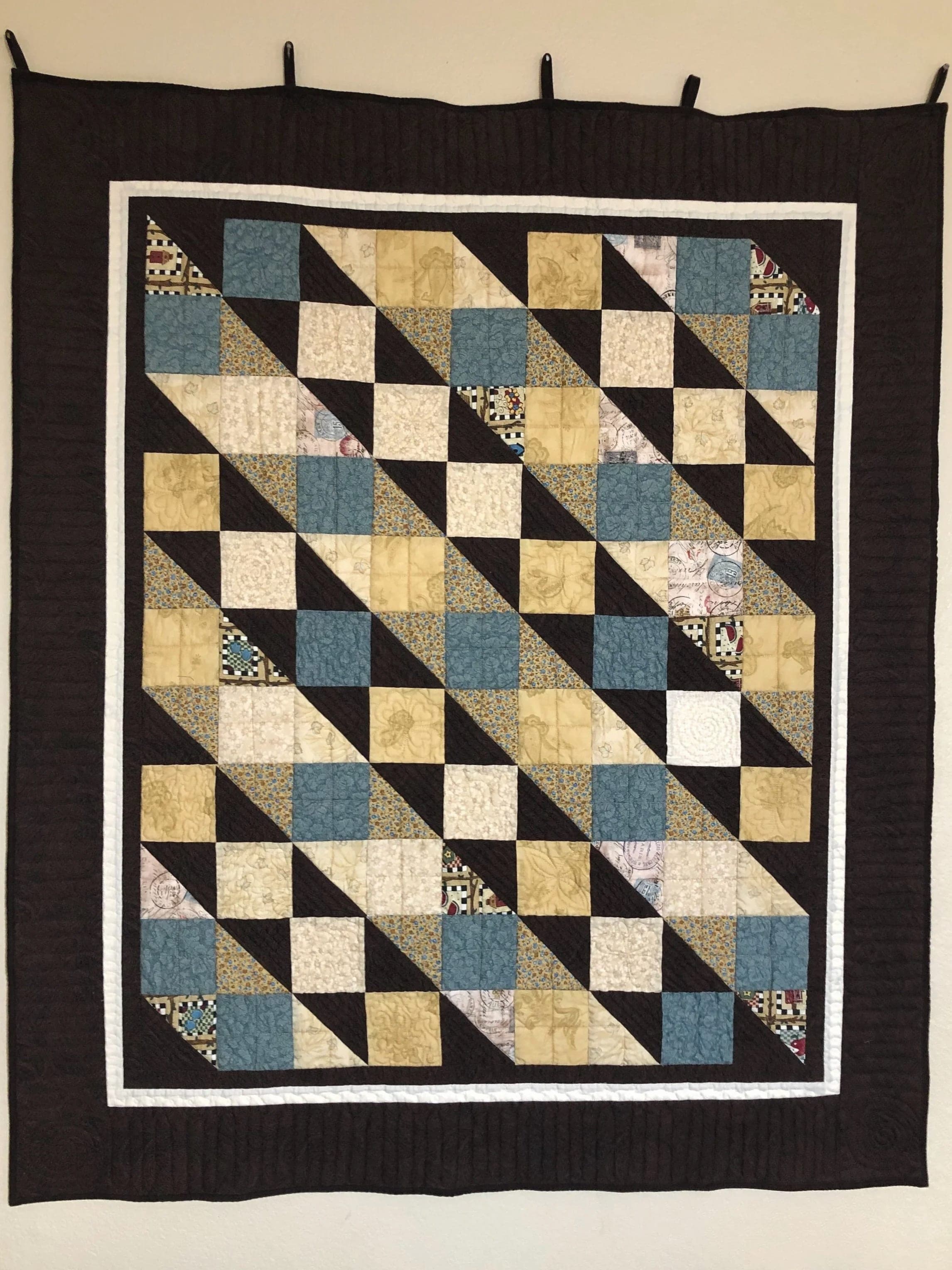 Quilt in black, gold and slate blue arranged in diagonal squares, on a dark background