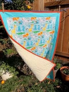 Quilt folded back to show a pastel animal print on one side and cream quilting on the other