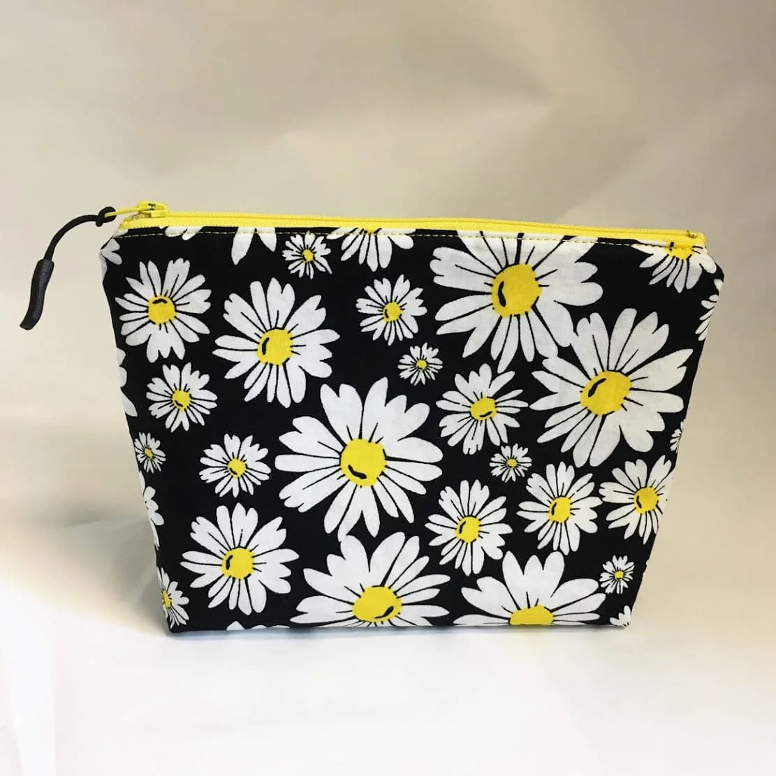 Boxed zip pouch in a black and white daisy print with a yellow zipper